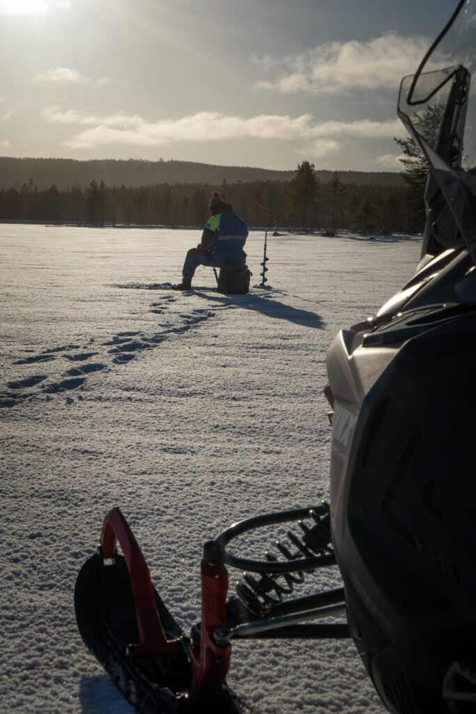 Een man aan het ijsvissen in de winter in zweden. Met de sneeuwscooter over het ijs